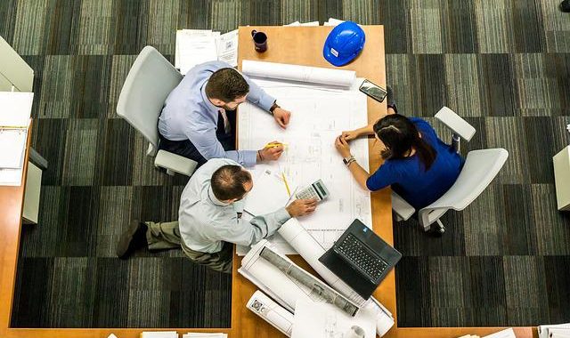 Reunión En Mesa De Trabajo De Dos Hombres Y Una Mujer Con Elementos De Oficina
